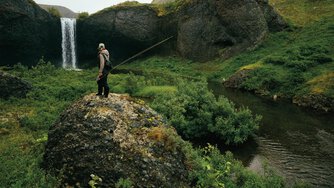 An angler scouts a remote waterfall from a distance.