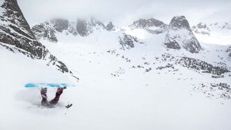 A snowboarder mid-fall with their head buried in the snow and their legs and board stretching up towards the sky.