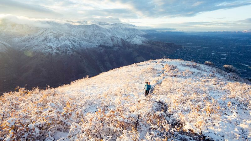 A runner on a trail climbing into snowy mountains.