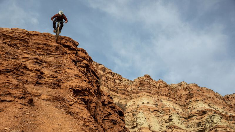 A mountain biker descends a steep route on red rocks.