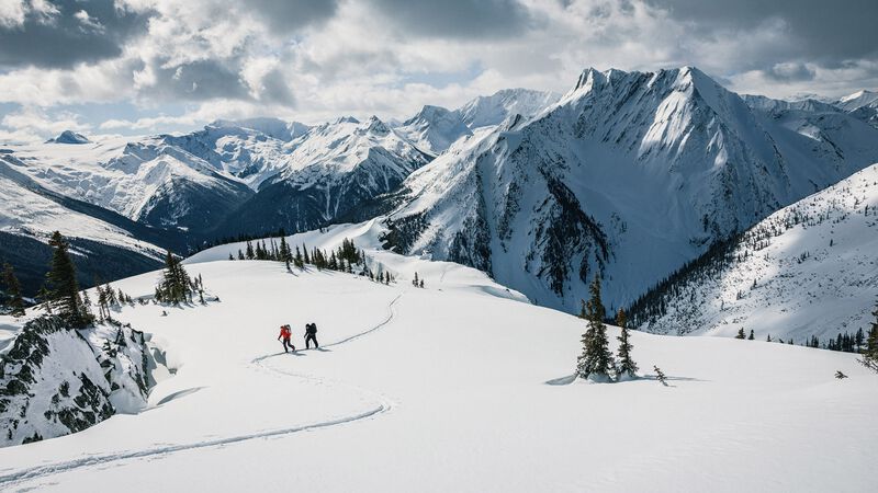 Two skiers heading up a skintrack in snowy mountains.